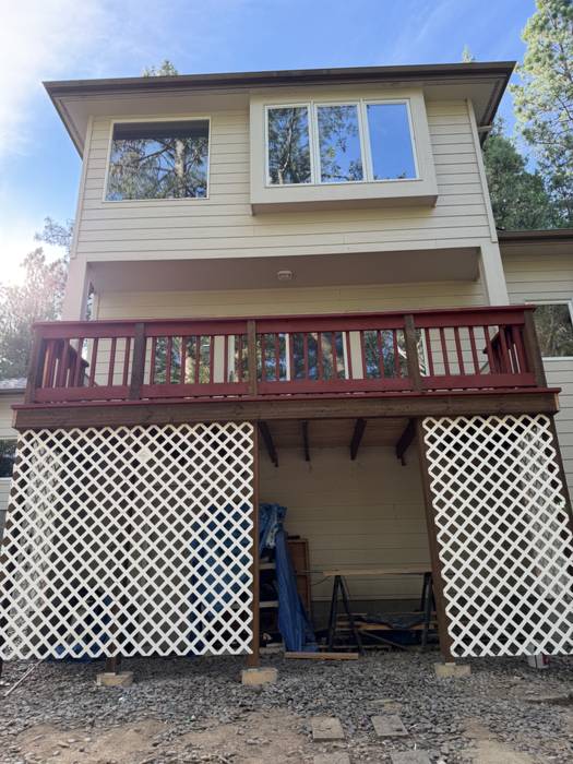 Full front view of a second-story deck with a red-stained wood railing above new white lattice skirting that screens the storage area below, at a home near Grants Pass, Oregon.