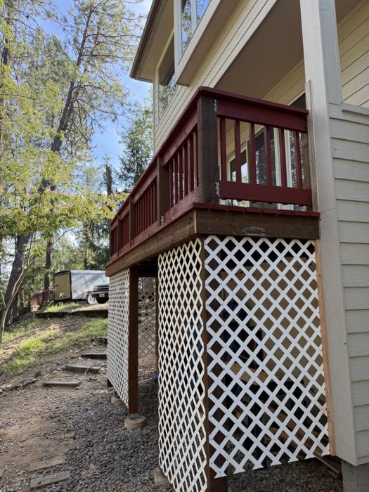 Close view of a second-story deck with red-stained rail posts and new white lattice skirting enclosing the space underneath at a wooded Southern Oregon home.