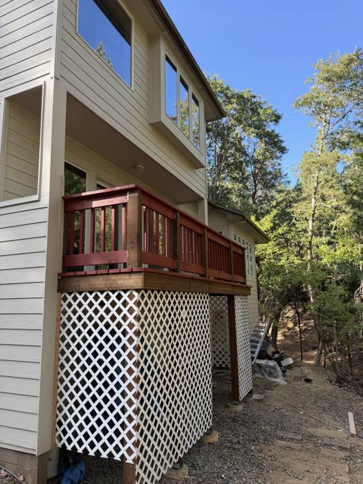 Elevated wood deck with a red-stained railing and white lattice skirting on a two-story home surrounded by pines in Southern Oregon.