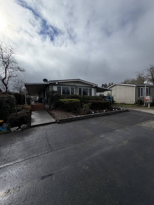 Manufactured home in Grants Pass, Oregon after a property cleanup, with the boundary hedge and foundation shrubs trimmed back square and the planting bed edges recut along the driveway.