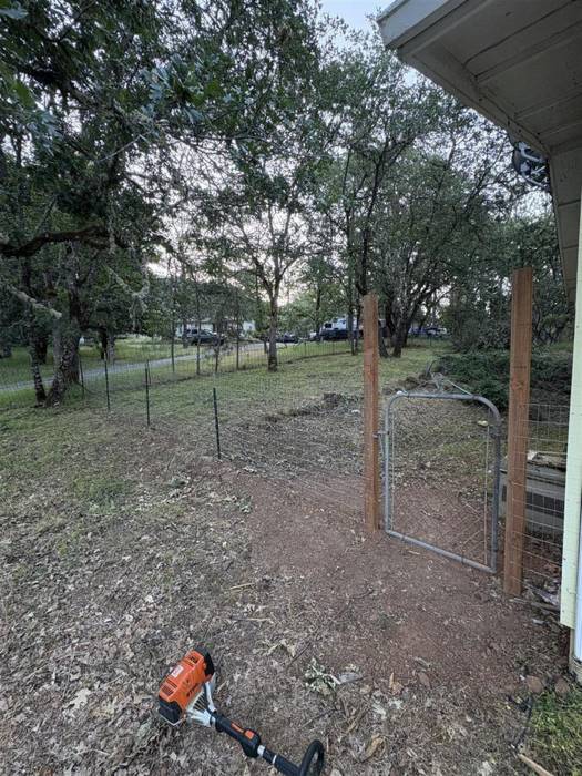 Wood-framed wire fence with a steel walk-through gate installed beside a house on a shaded Southern Oregon property.
